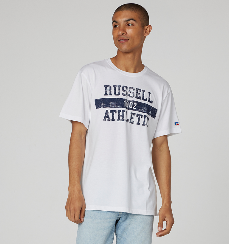 Male model wearing a white graphic Russell Athletic tee. 